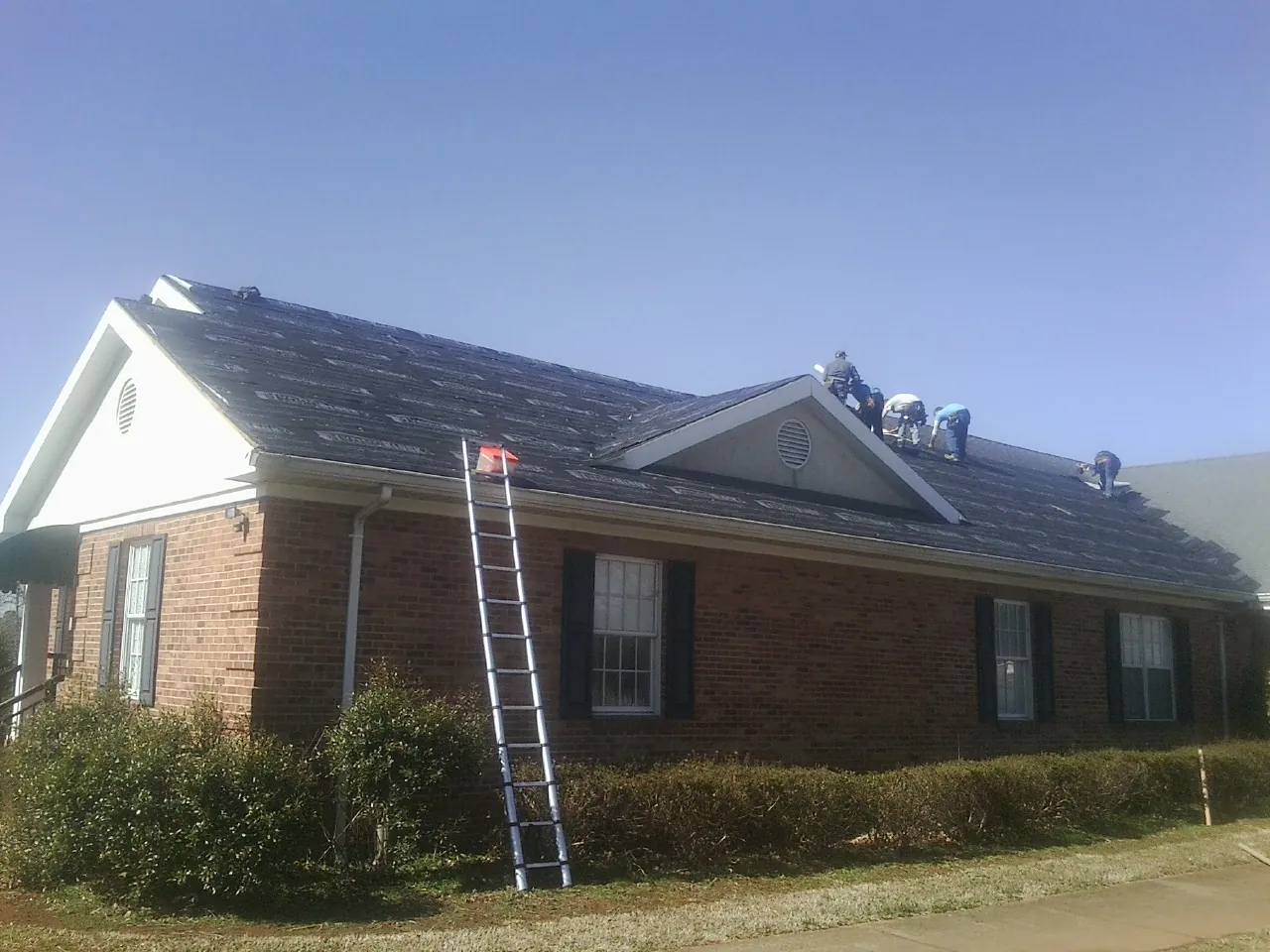 Crew tearing shingles off a brick ranch roof with a ladder set — Emergency Roof Repair work by our crew in Eatontown