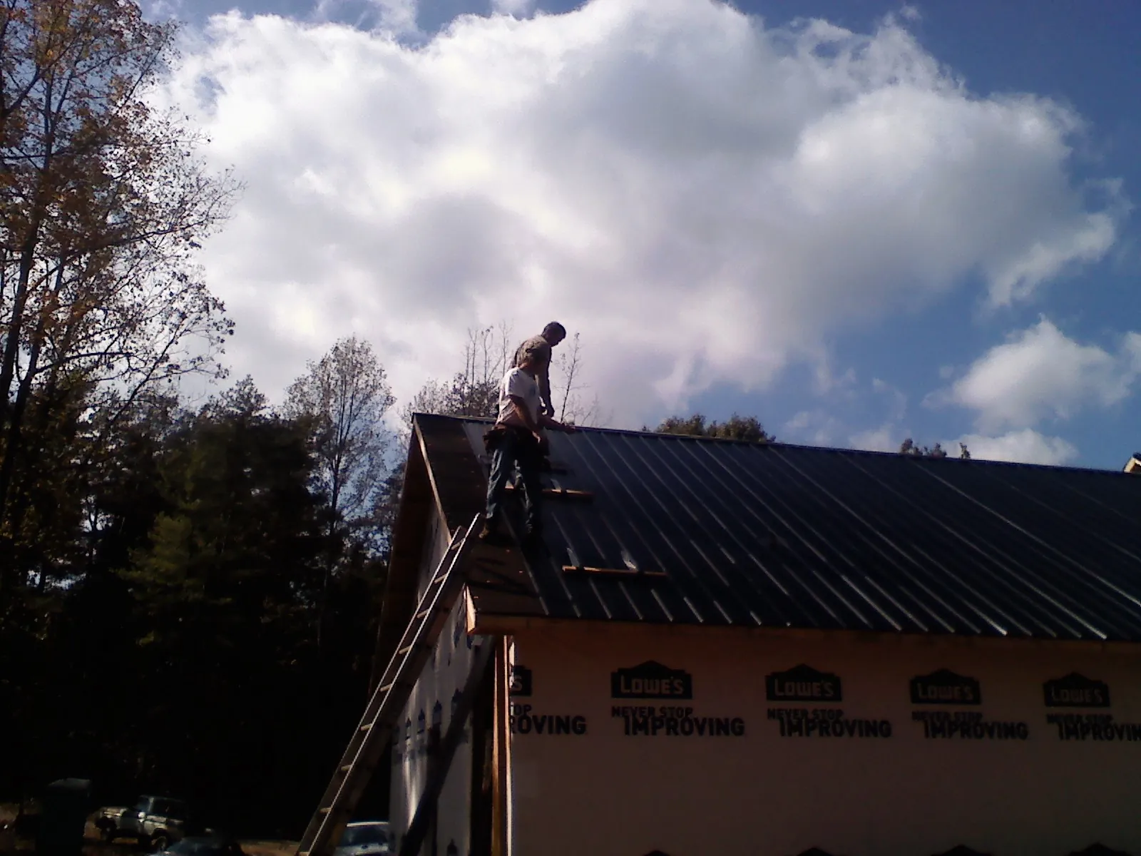 Roofer fastening dark metal panels high against a cloudy sky, from a Roof Inspection job in Eatontown