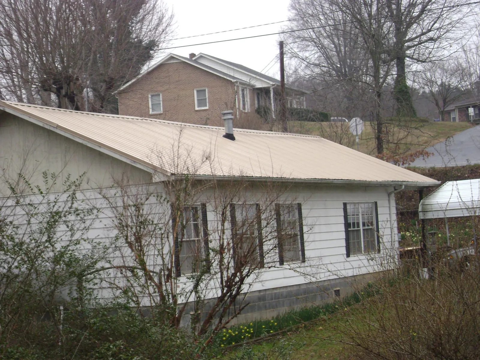 Tan metal roof on a white sided house set into a hillside — Commercial Roofing by Roofing Brothers in Eatontown